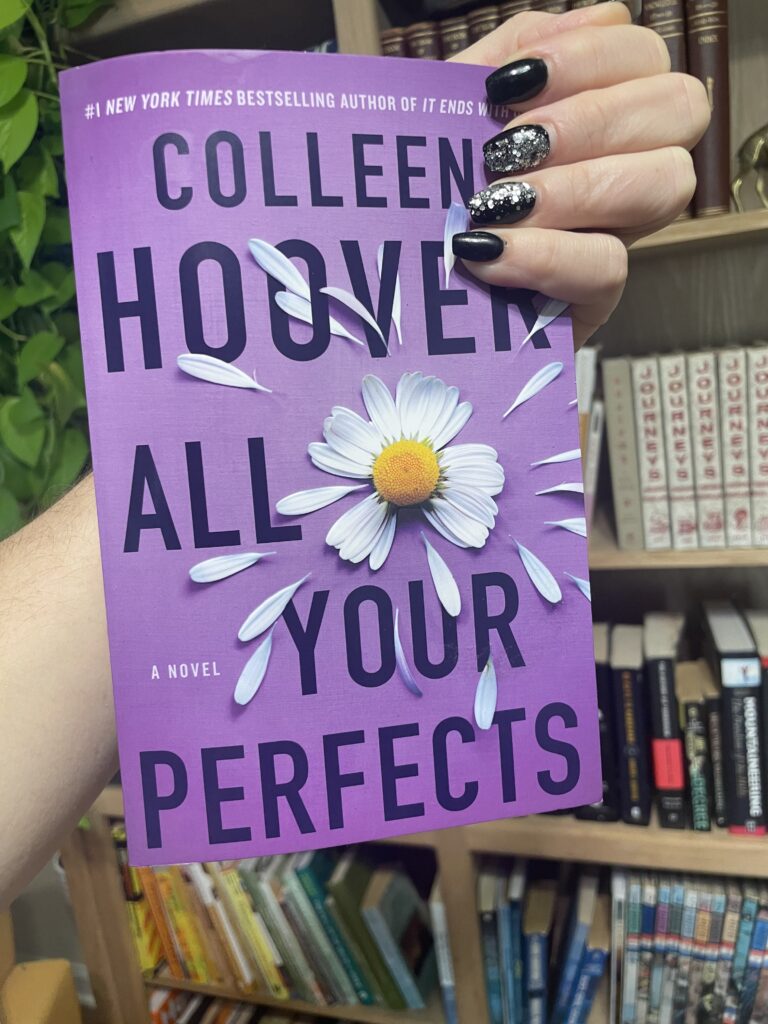 All Your Perfects book cover being held in front of a bookcase.