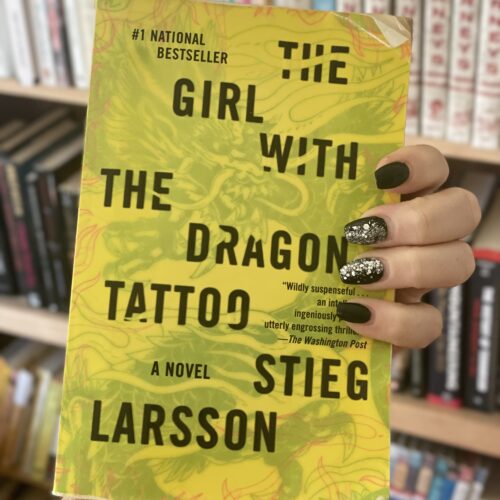 hand holding the book Girl with the Dragon tattoo in front of a bookshelf