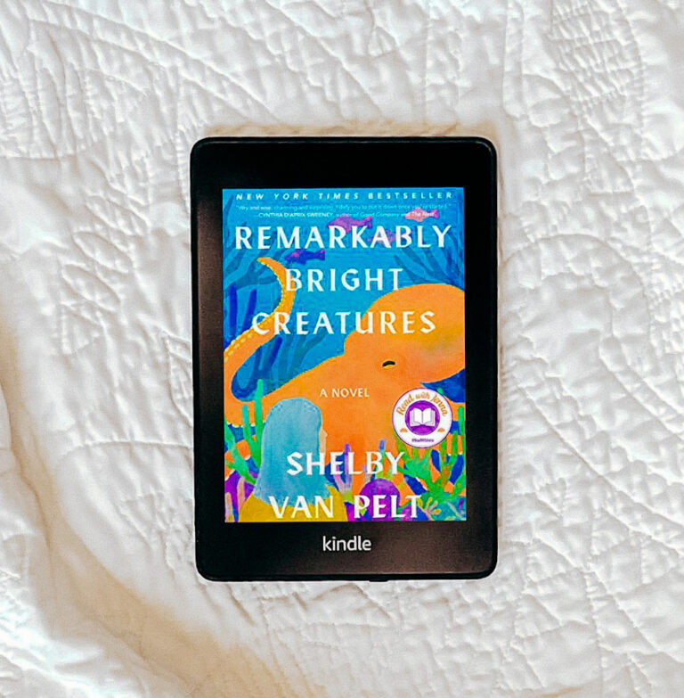 the book Remarkably Bright Creatures on a white quilt featured on a Kindle.